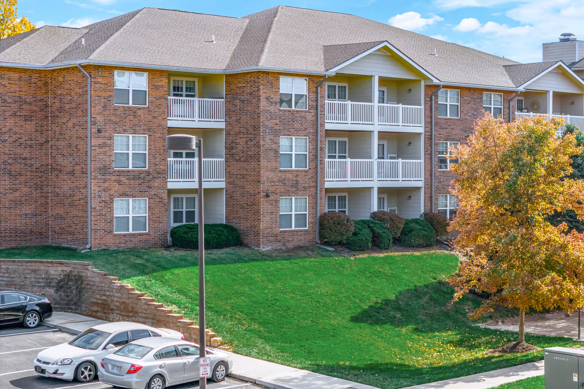Rosewood Place exterior: brick senior living building with balconies, green lawn, and parked cars.