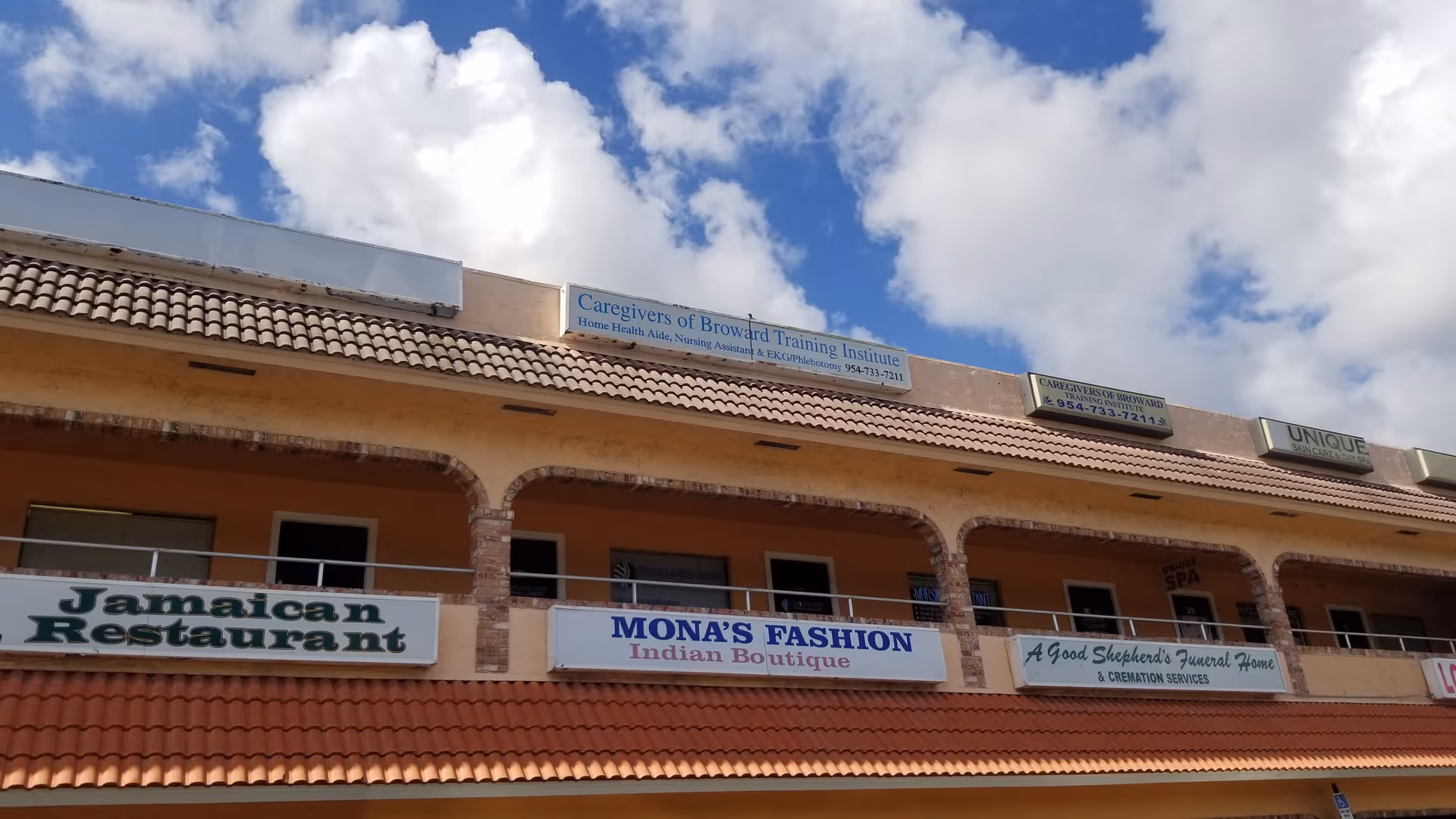 Orange two-story building with arched balconies and multiple storefront signs against a blue sky.