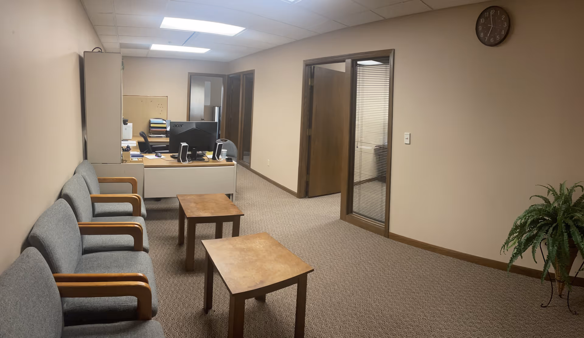 Office waiting area with chairs along the wall, a desk, and a plant.