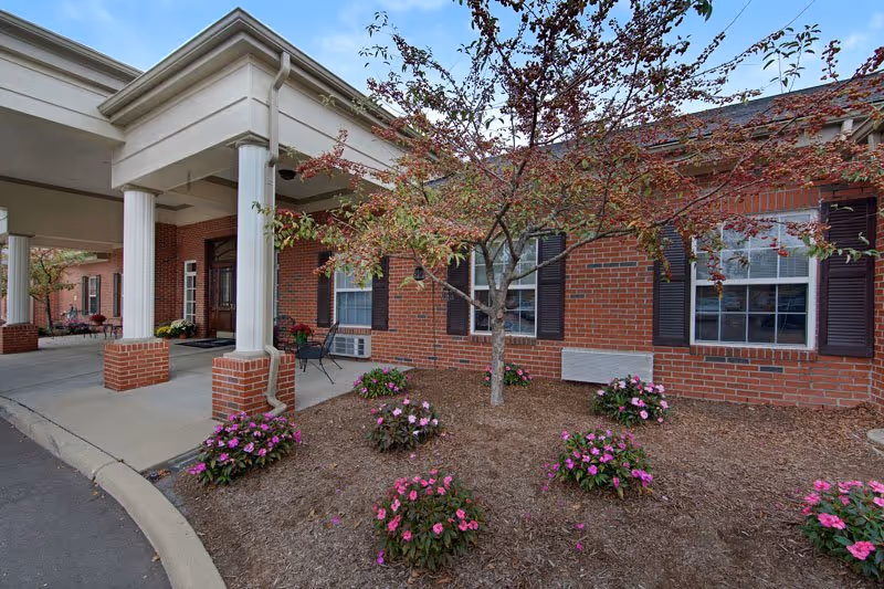 Brick senior living facility exterior with a covered entrance and landscaped front garden.