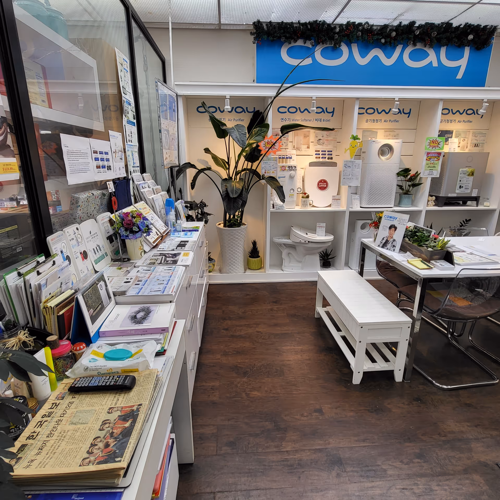 Indoor showroom with white shelves displaying Coway air purifiers, plants, and a waiting bench.