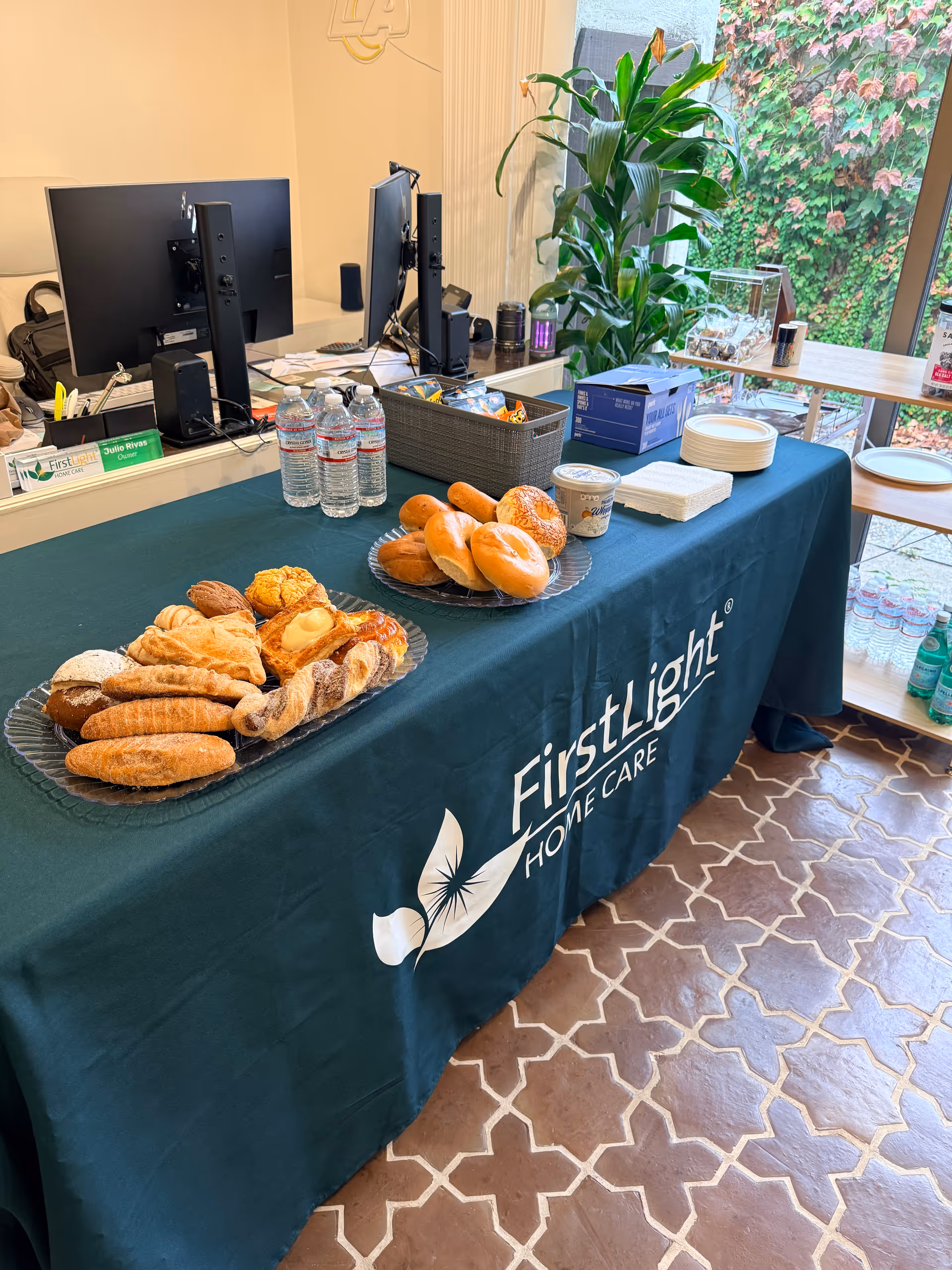 Indoor reception area with a FirstLight Home Care table, pastries, water, and computers.