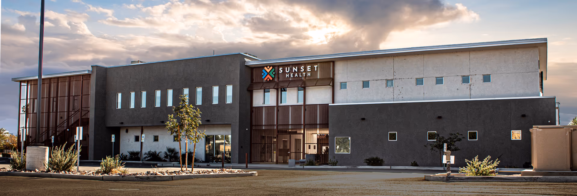 Modern Sunset Health facility exterior with dark gray facade and parking lot.
