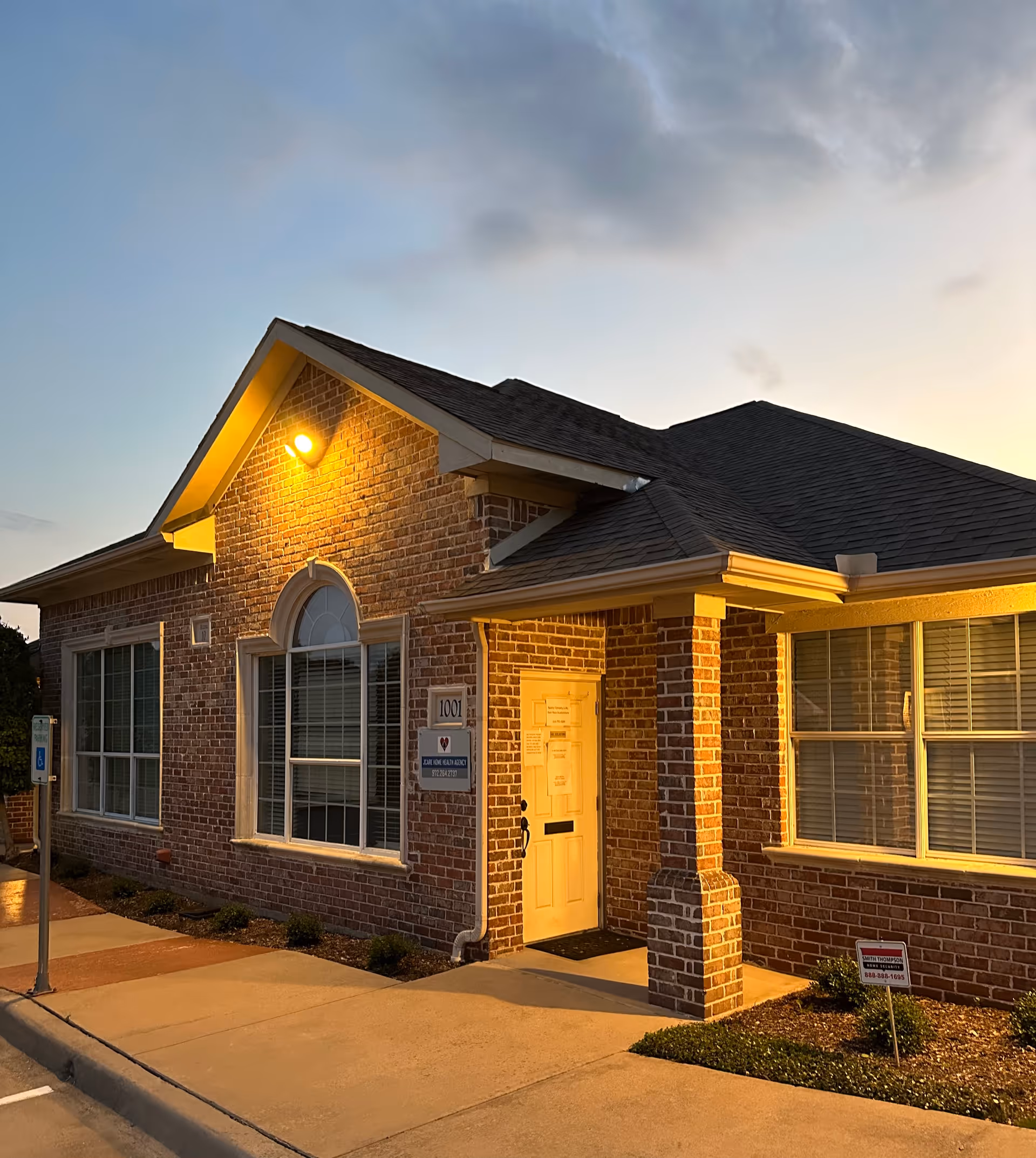 Brick facility exterior with a front entrance and large windows at dusk.