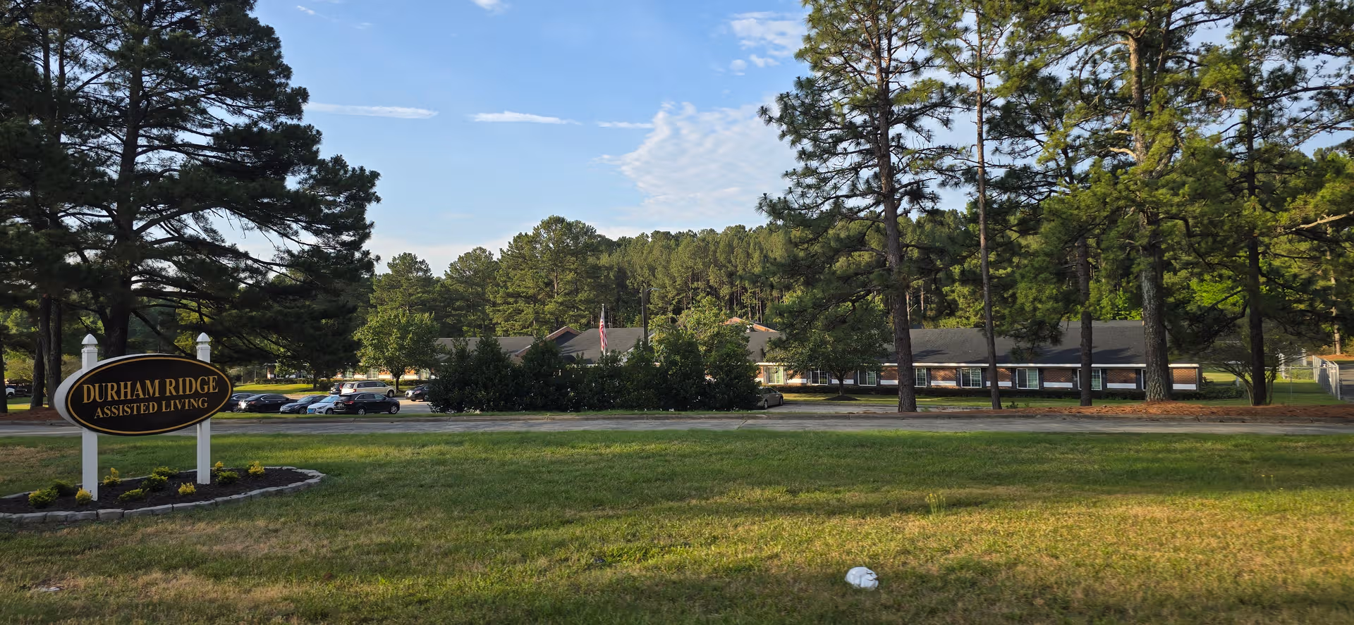 Exterior view of Durham Ridge Assisted Living with a sign, parking lot, and trees