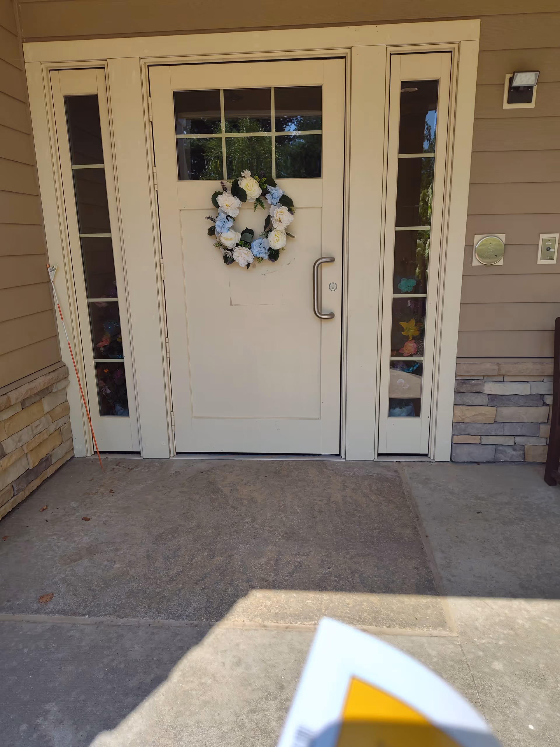 Front door with a floral wreath flanked by narrow sidelights on a stone porch.