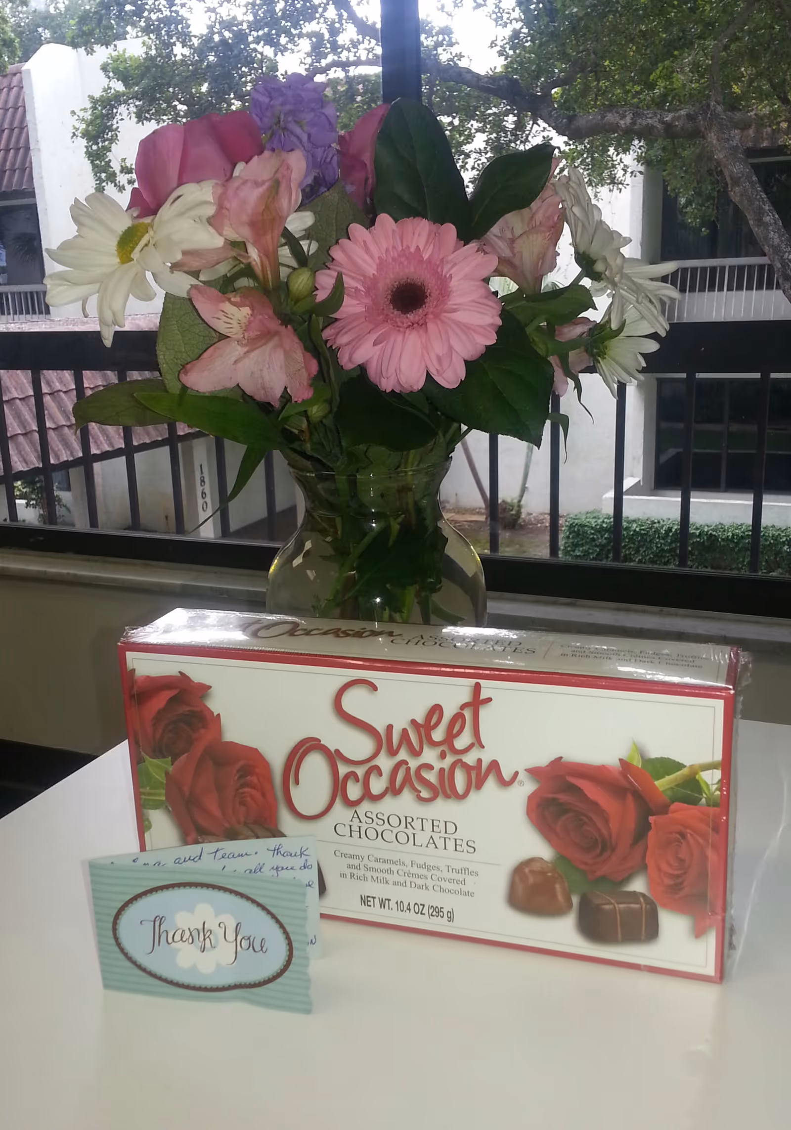 Bouquet of pink and white flowers in a glass vase beside a chocolate box.