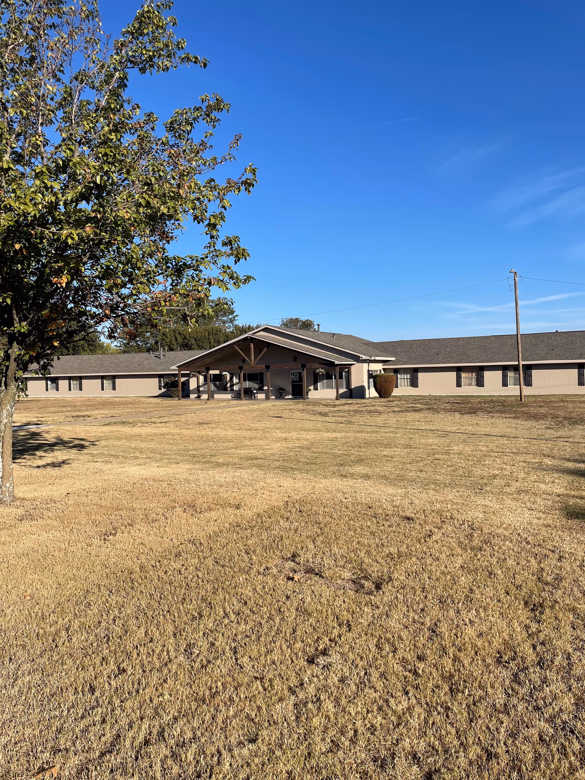 A single-story beige senior living facility with a covered entrance and expansive front lawn.