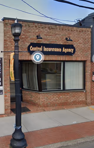 Brick storefront with Central Insurance Agency sign and large front window along sidewalk.