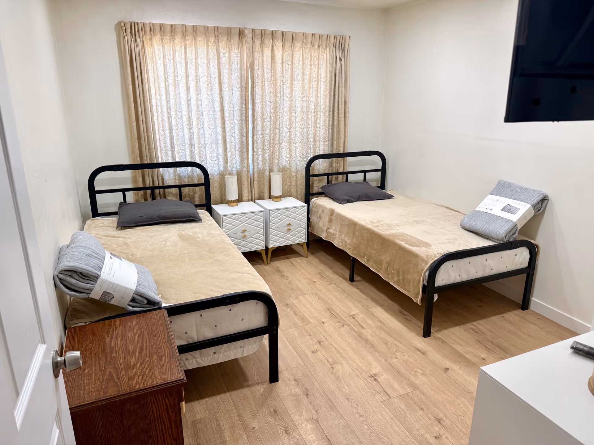 Two single beds with black frames flank a central nightstand in a compact bedroom.