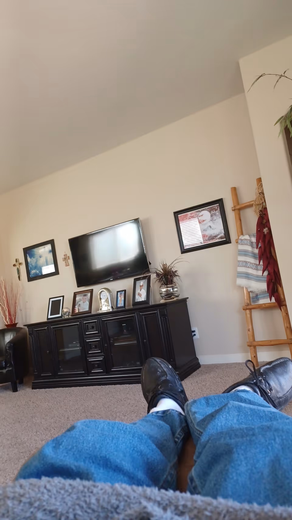 View of a living room with a television, dark cabinet, photos, and a ladder-style coat rack.