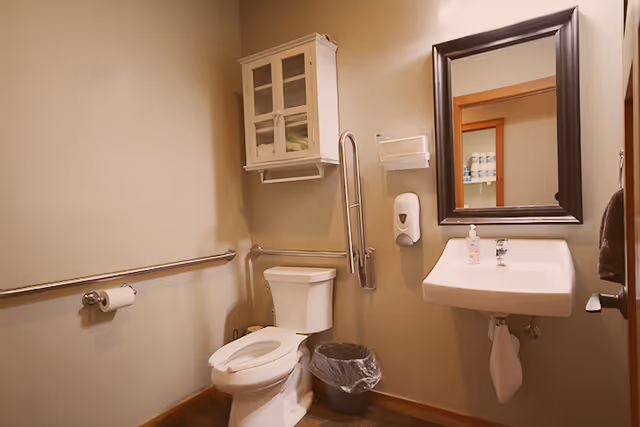 Accessible bathroom with toilet, sink, mirror, and grab bars.