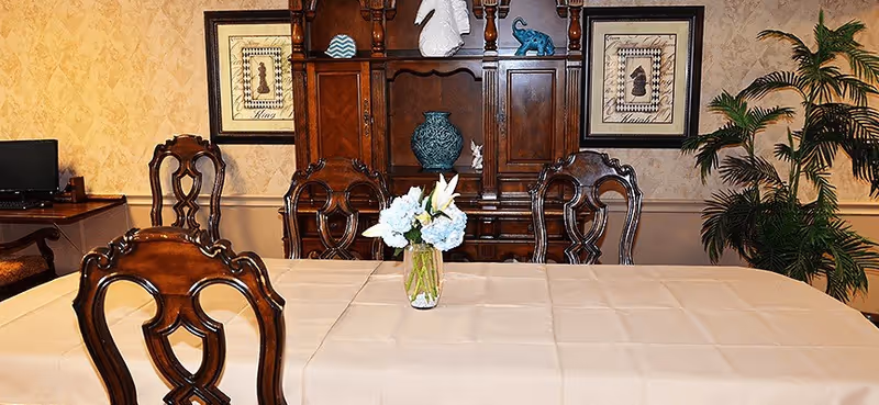 Formal dining room with beige table, ornate wooden chairs, and a large cabinet.
