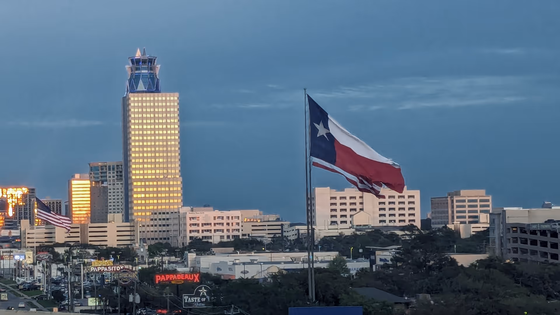 City skyline with tall buildings and a waving Texas flag in foreground.