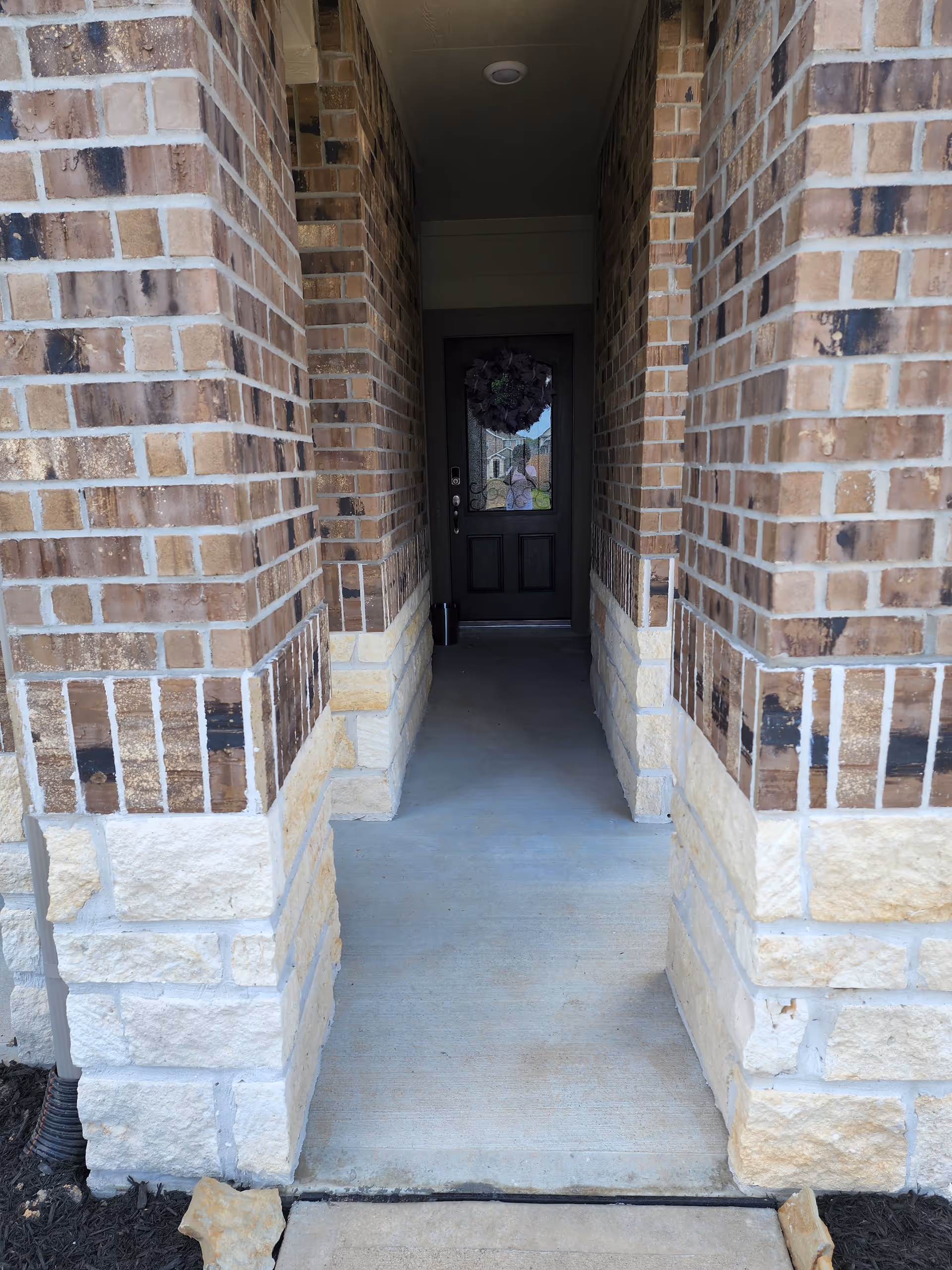 Brick building entrance with a covered walkway leading to a dark front door.