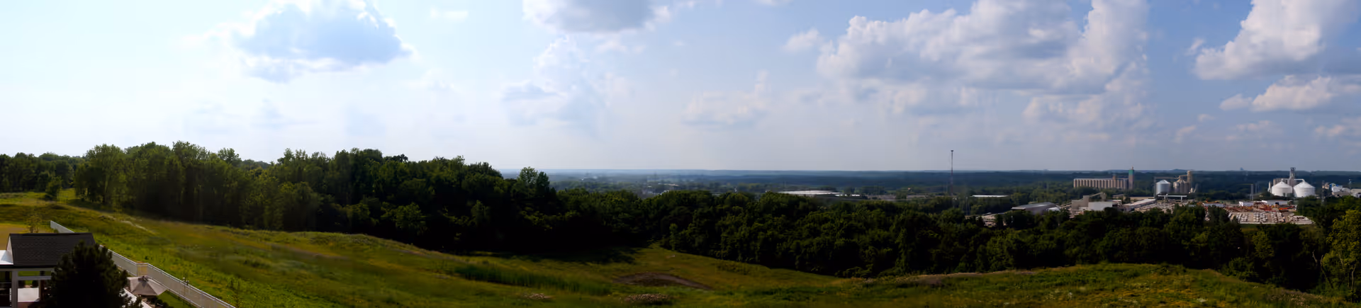 Wide panoramic outdoor landscape with grassy hills, trees, and distant buildings.