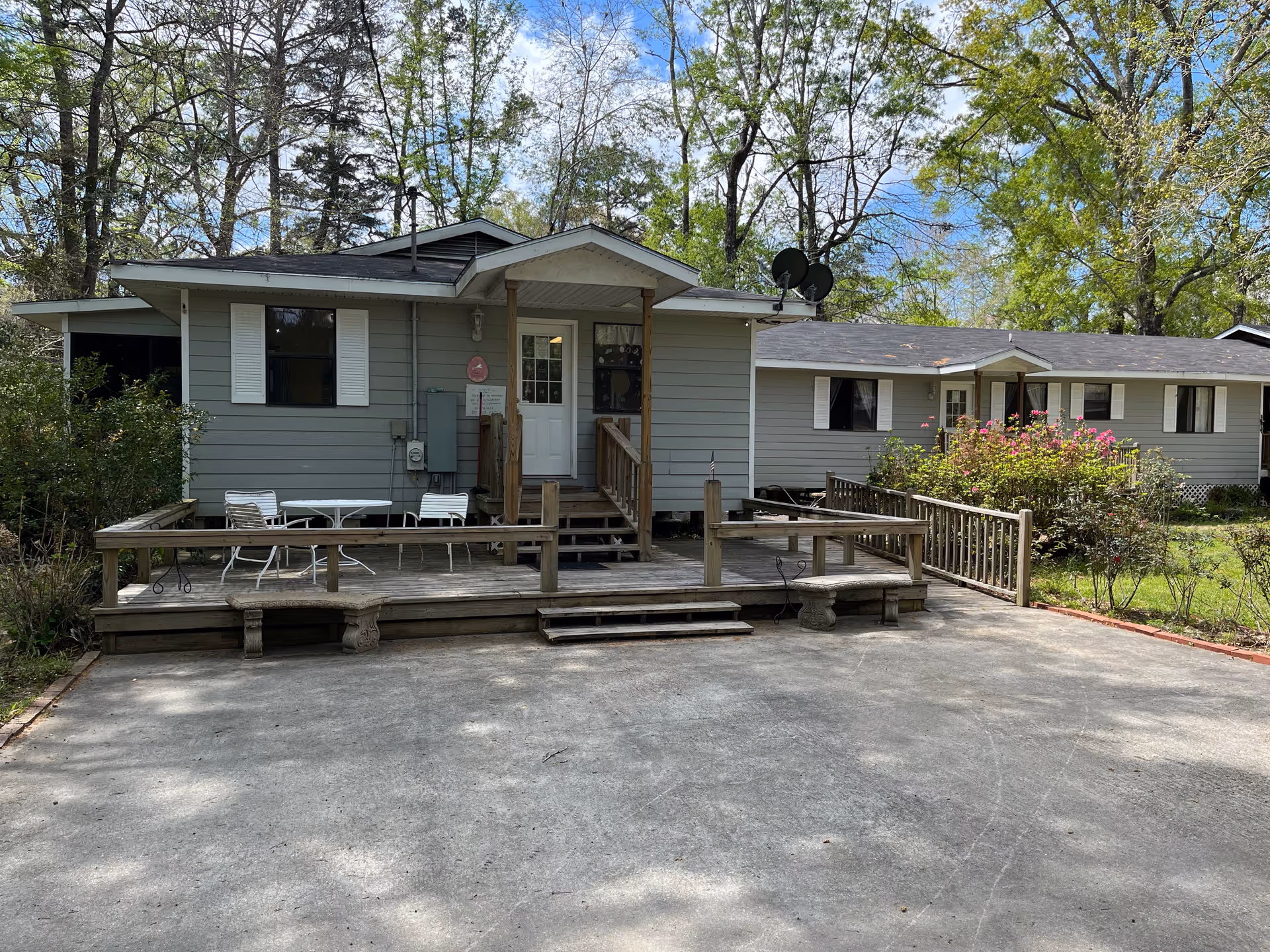 Gray, single-story facility with a wooden deck, outdoor seating, and surrounding trees.