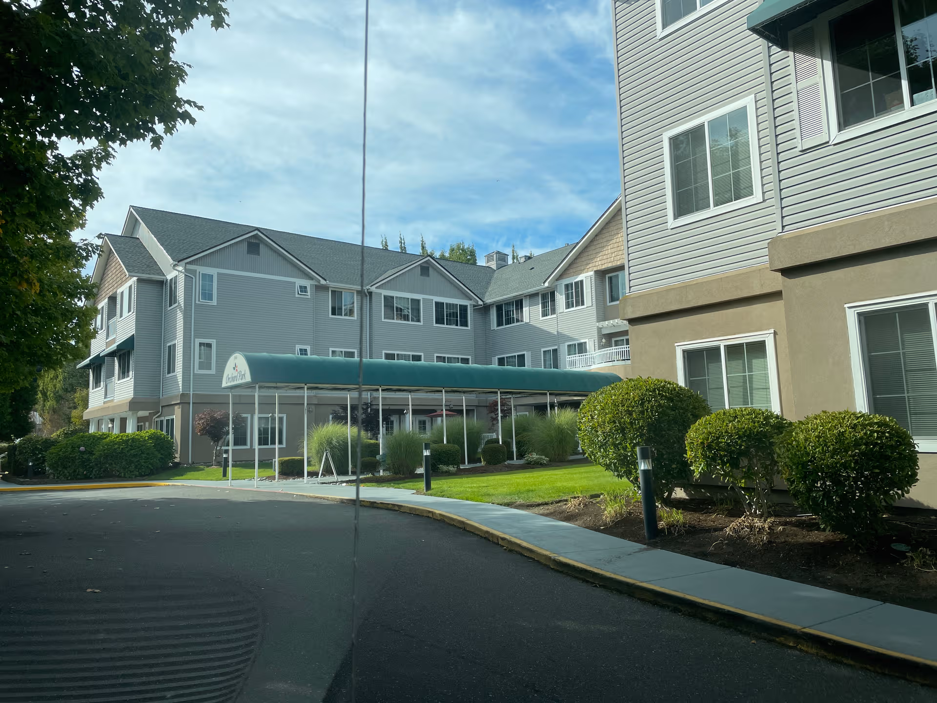 Exterior view of Orchard Park senior living building with a green canopy and landscaped entrance.