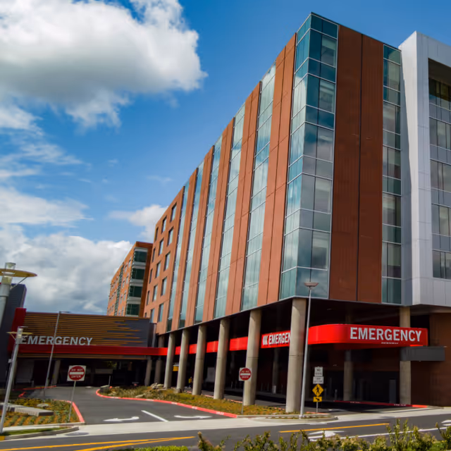 Modern multi-story hospital building with red emergency entrance signs.