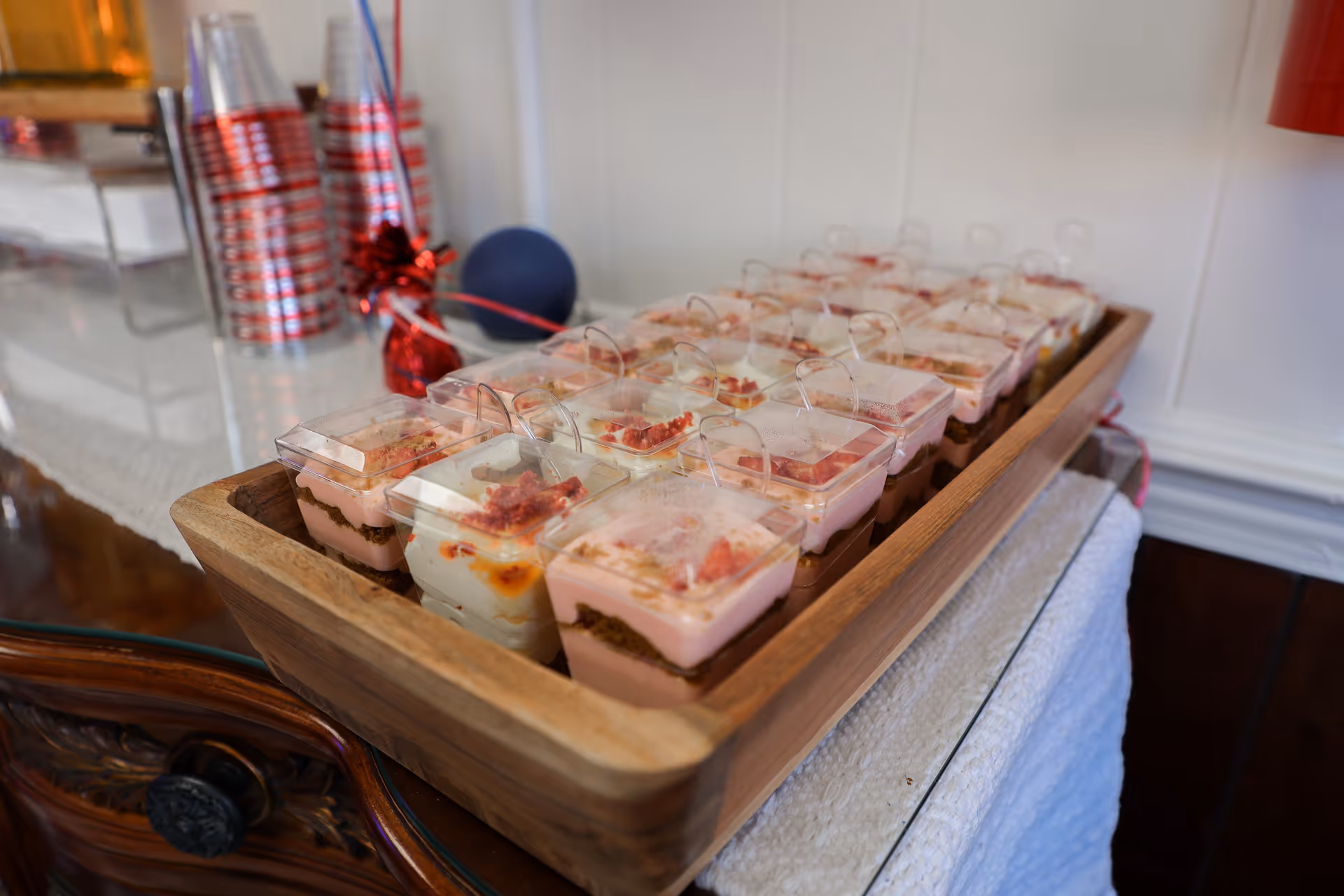 Wooden tray of small layered desserts with clear lids on a serving table.