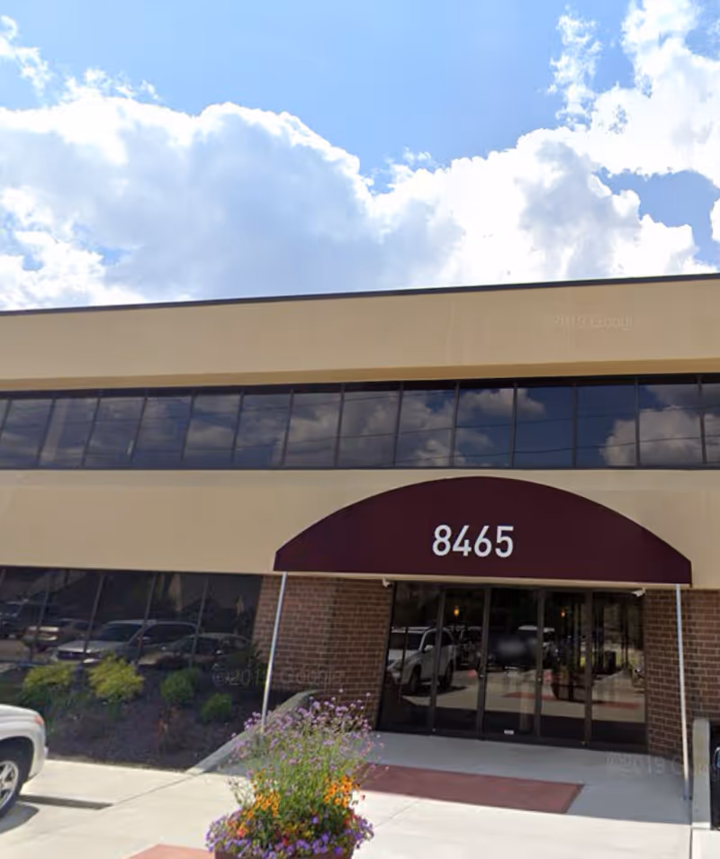 Exterior view of a beige building with a maroon awning and front entrance.