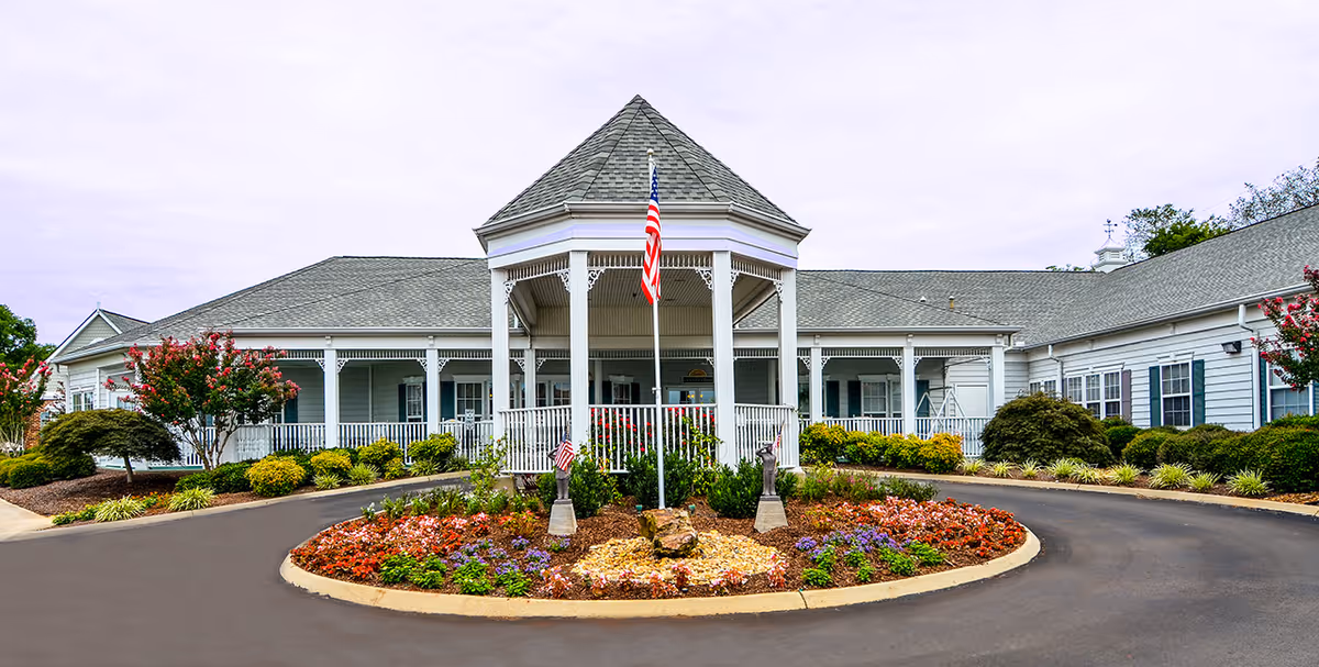 A circular driveway frames a central flower bed and white building with a peaked gazebo entrance.