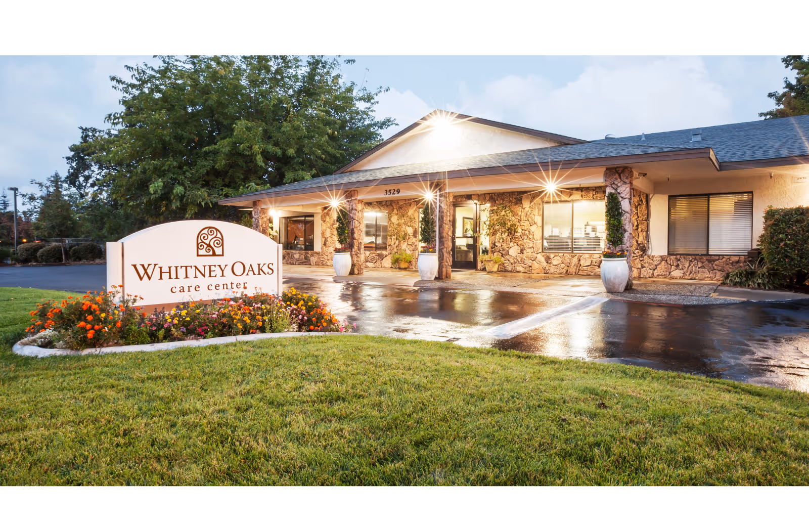 Exterior view of Whitney Oaks Care Center entrance with stone facade and landscaped sign.