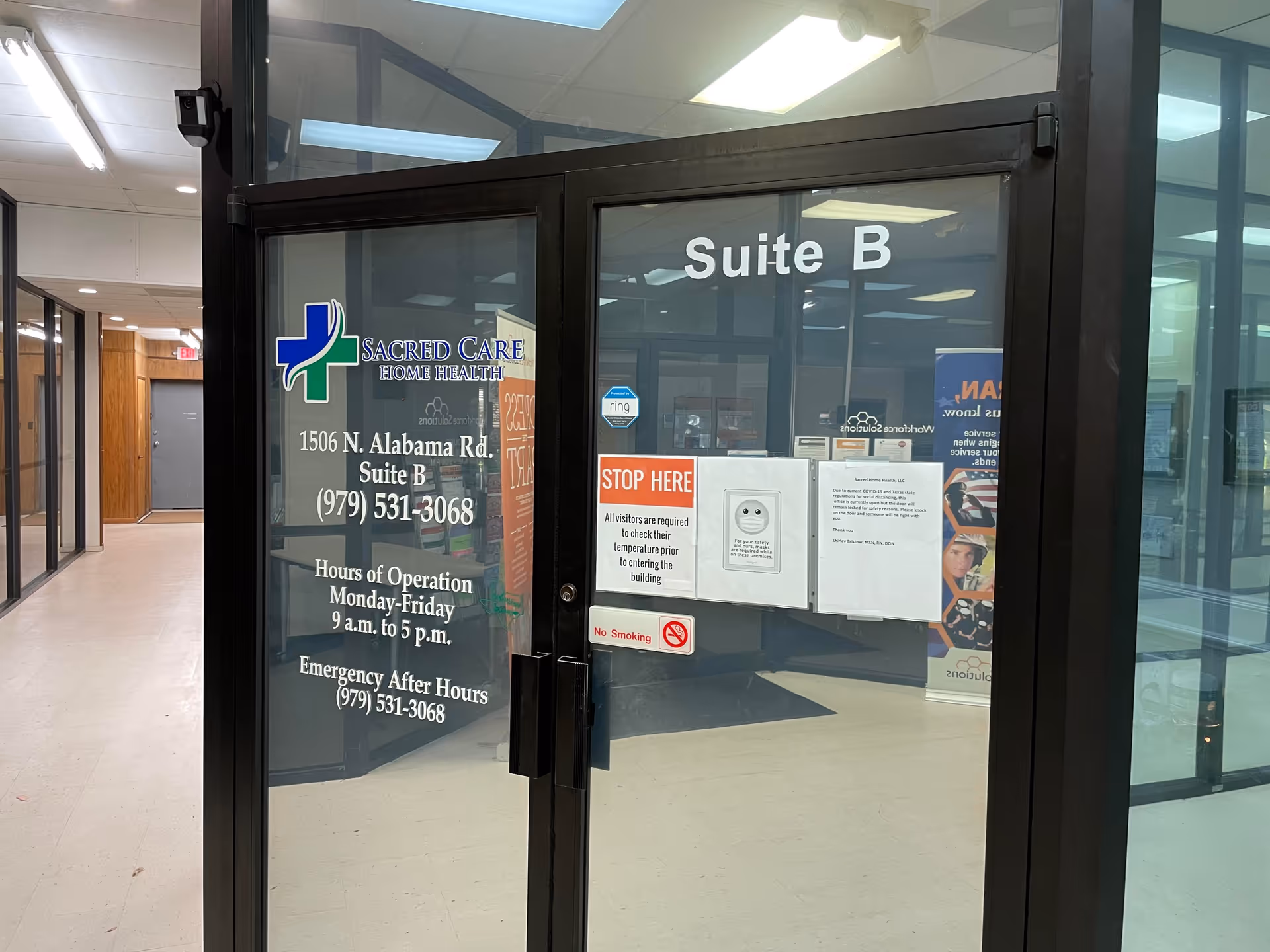 Glass doors show Suite B with Sacred Care Home Health signage inside a corridor.