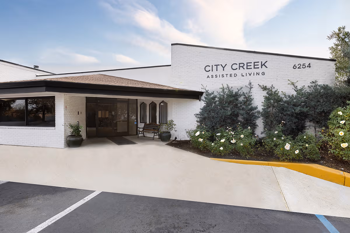 White brick facility entrance labeled City Creek Assisted Living with shrubs and parking