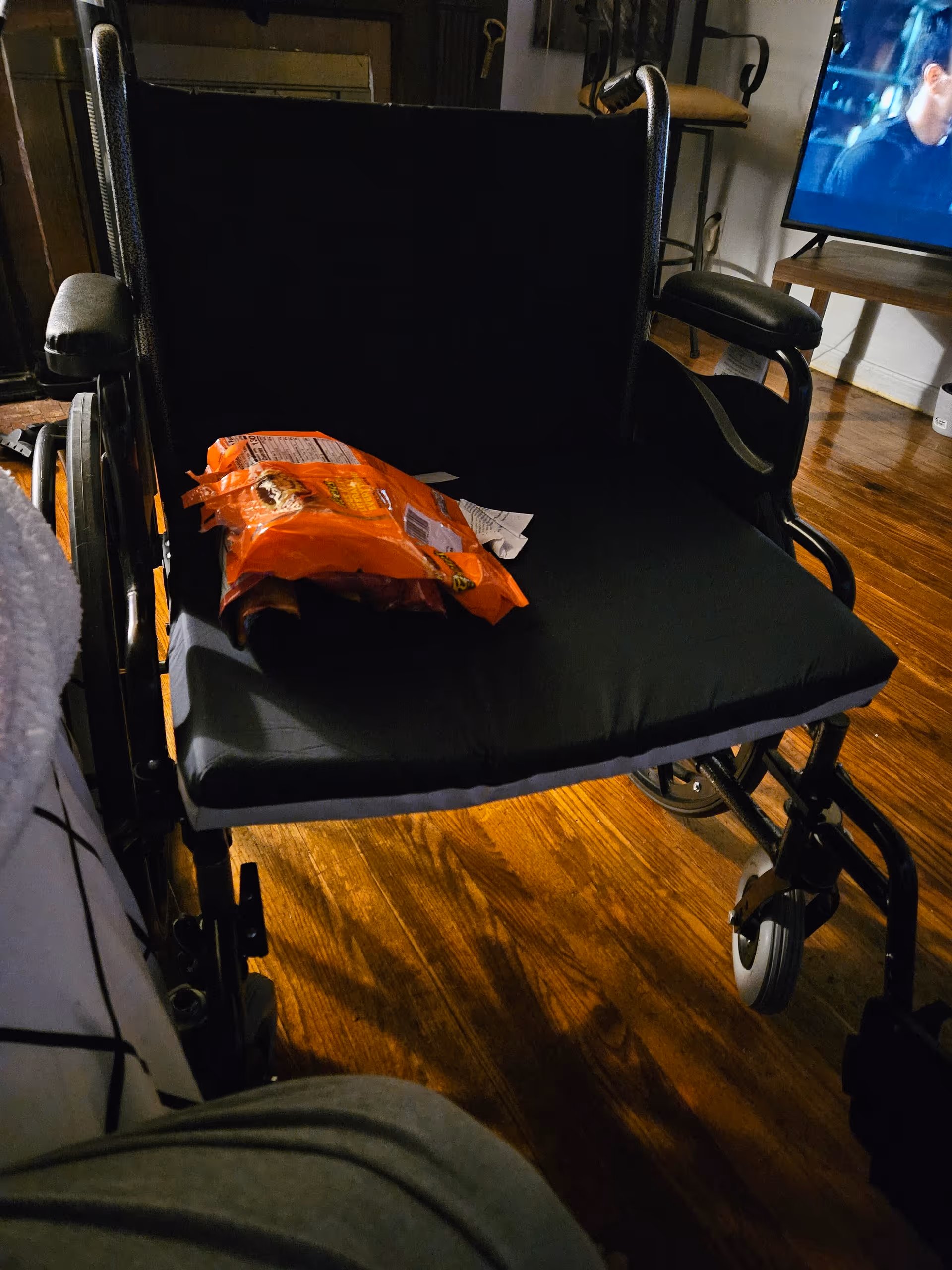 A wheelchair sits in a dimly lit living area with a TV in the background.