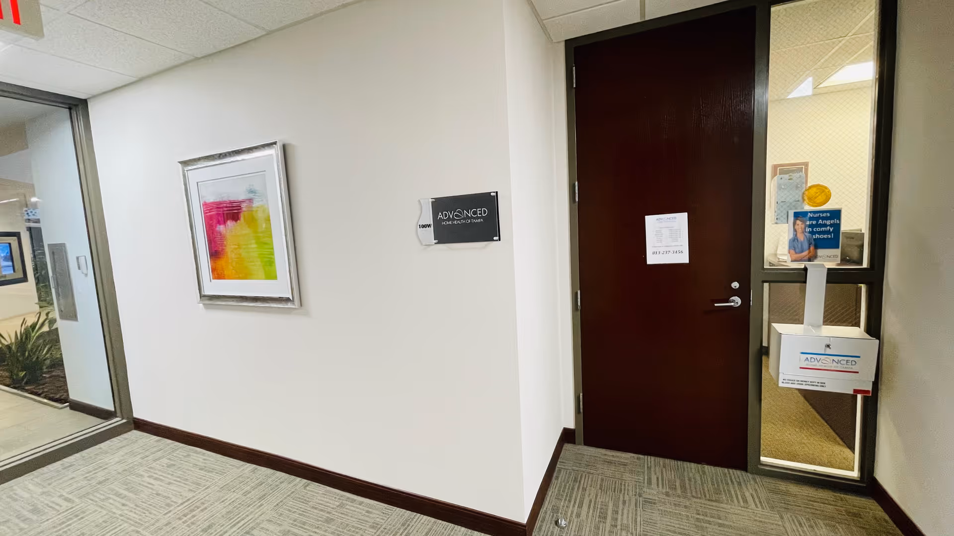 Interior hallway of a senior facility with a closed dark wood door and framed artwork.