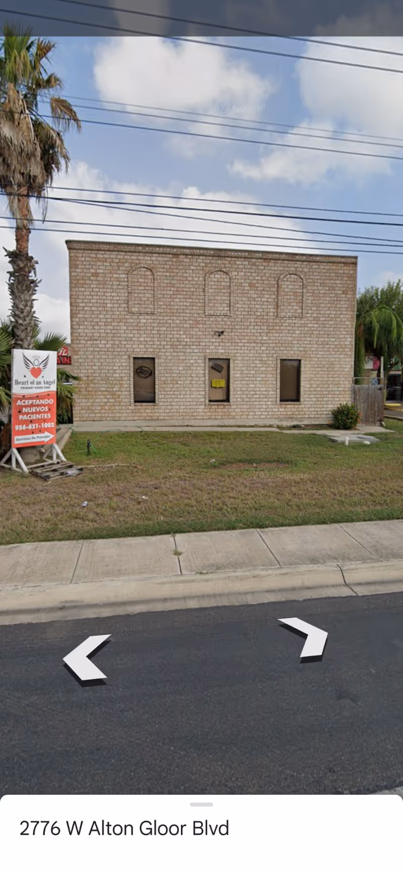 Brick building on a street with palm trees and a nearby sign.