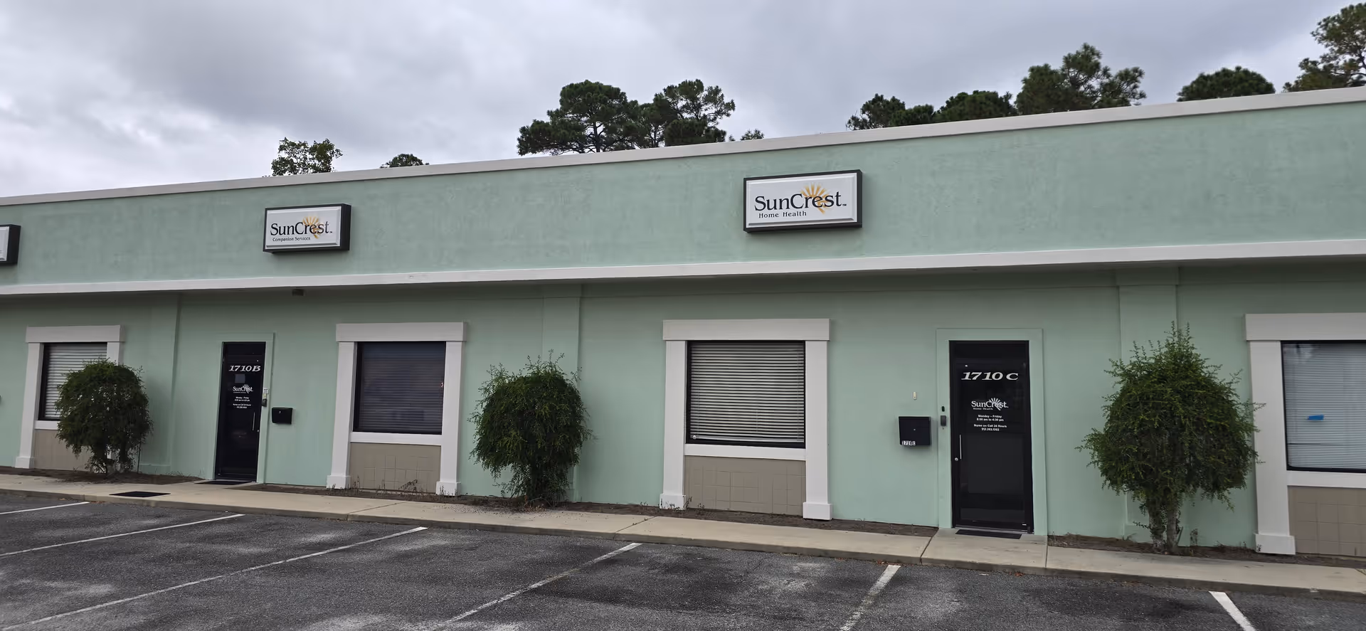 Mint green SunCrest building exterior with signage, windows, doors, and trimmed shrubs.