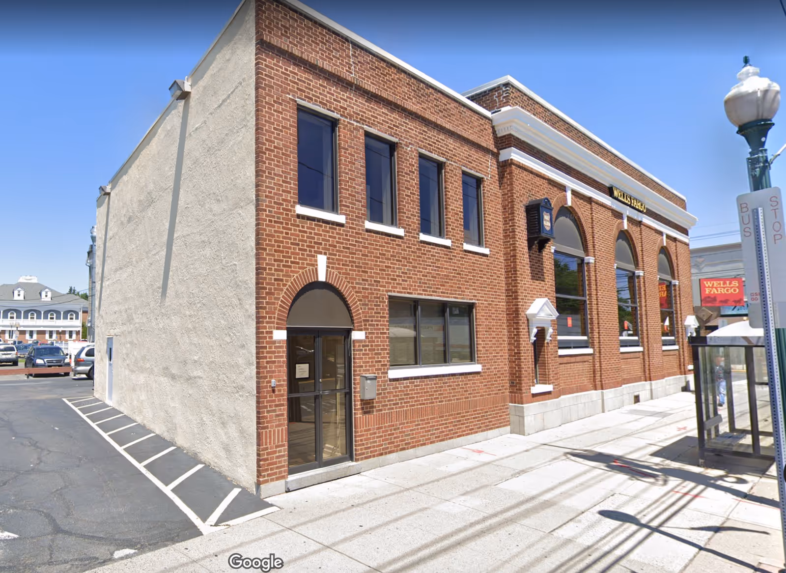 Brick building exterior with arched windows on a sunny street.