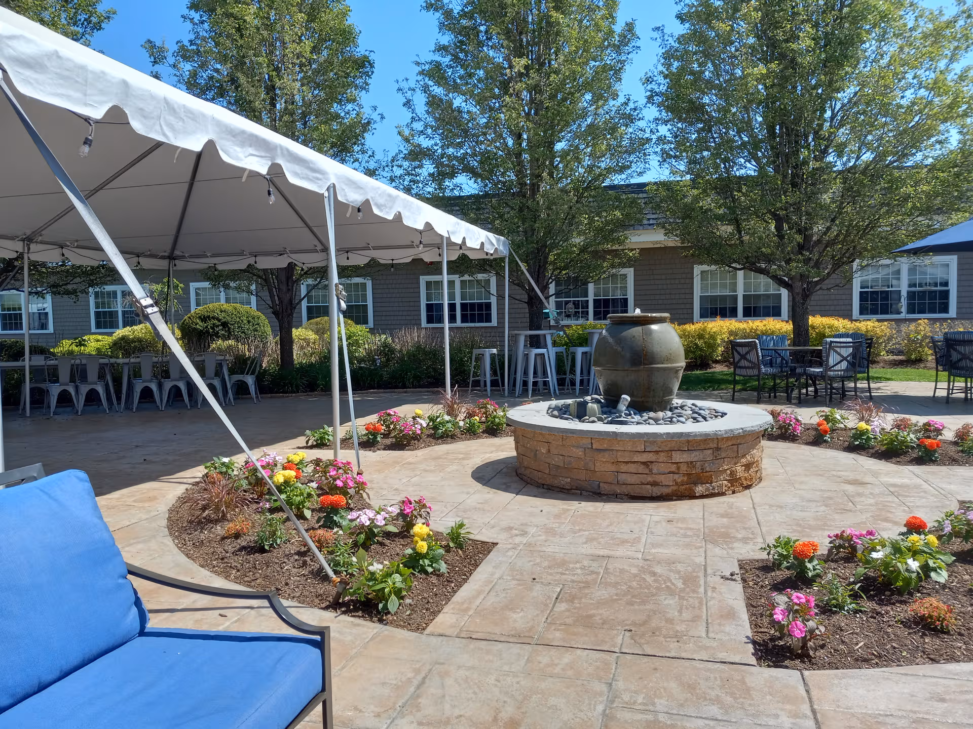 Outdoor courtyard with a stone fountain, flower beds, and seating under a canopy.