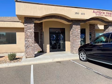 Exterior view of a building entrance with stone columns and a parked black SUV.