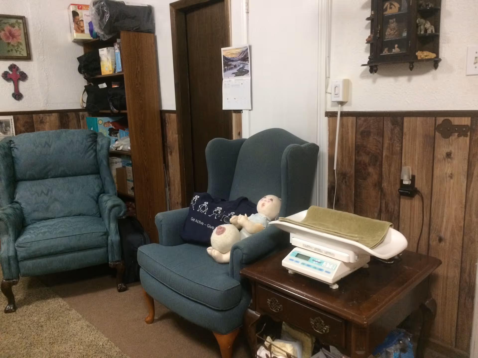 Cozy living room with green chairs, wood paneling, and a baby scale on a table.