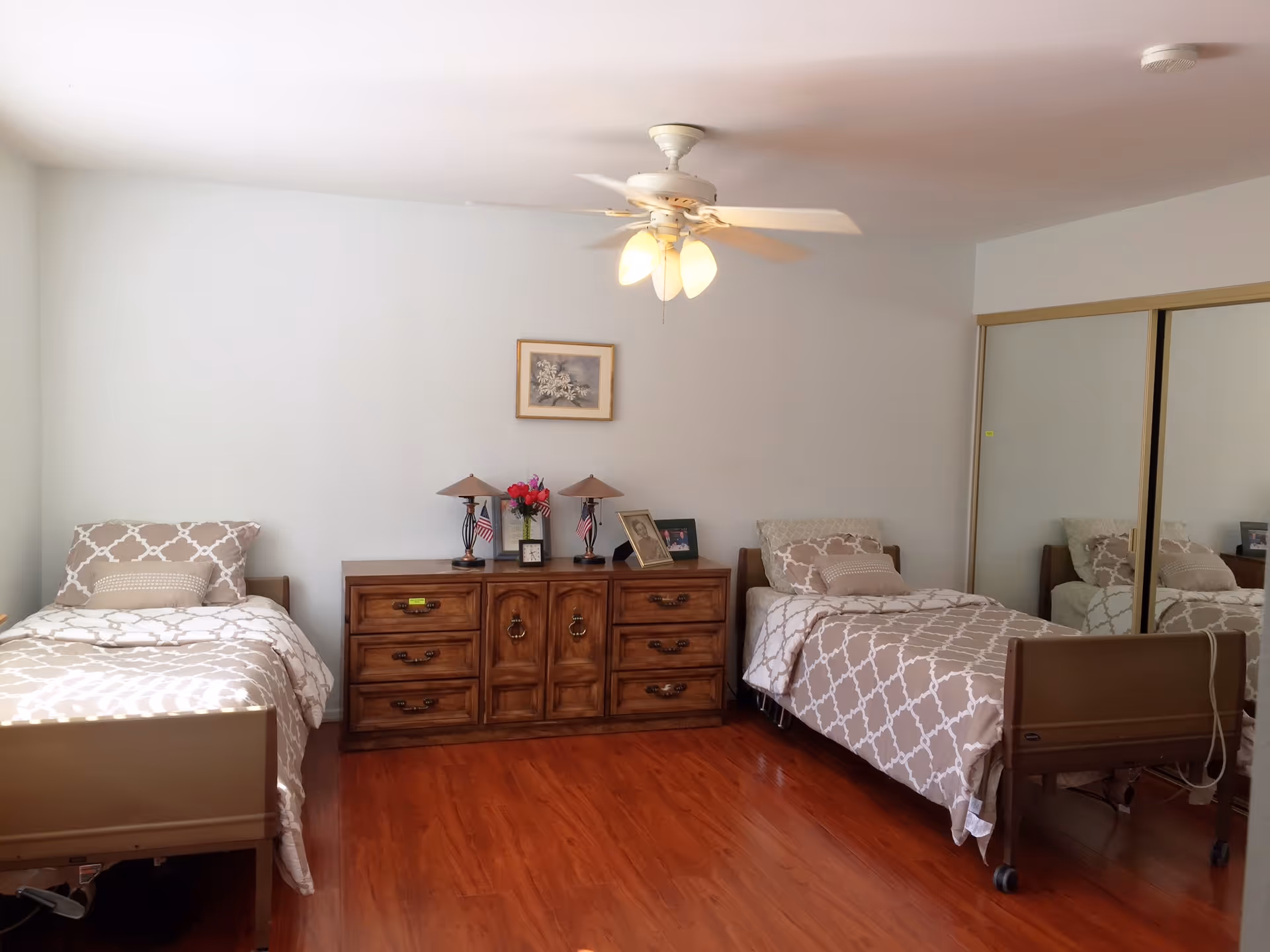 Two single beds, a dresser, and a mirrored closet in a shared senior living bedroom.