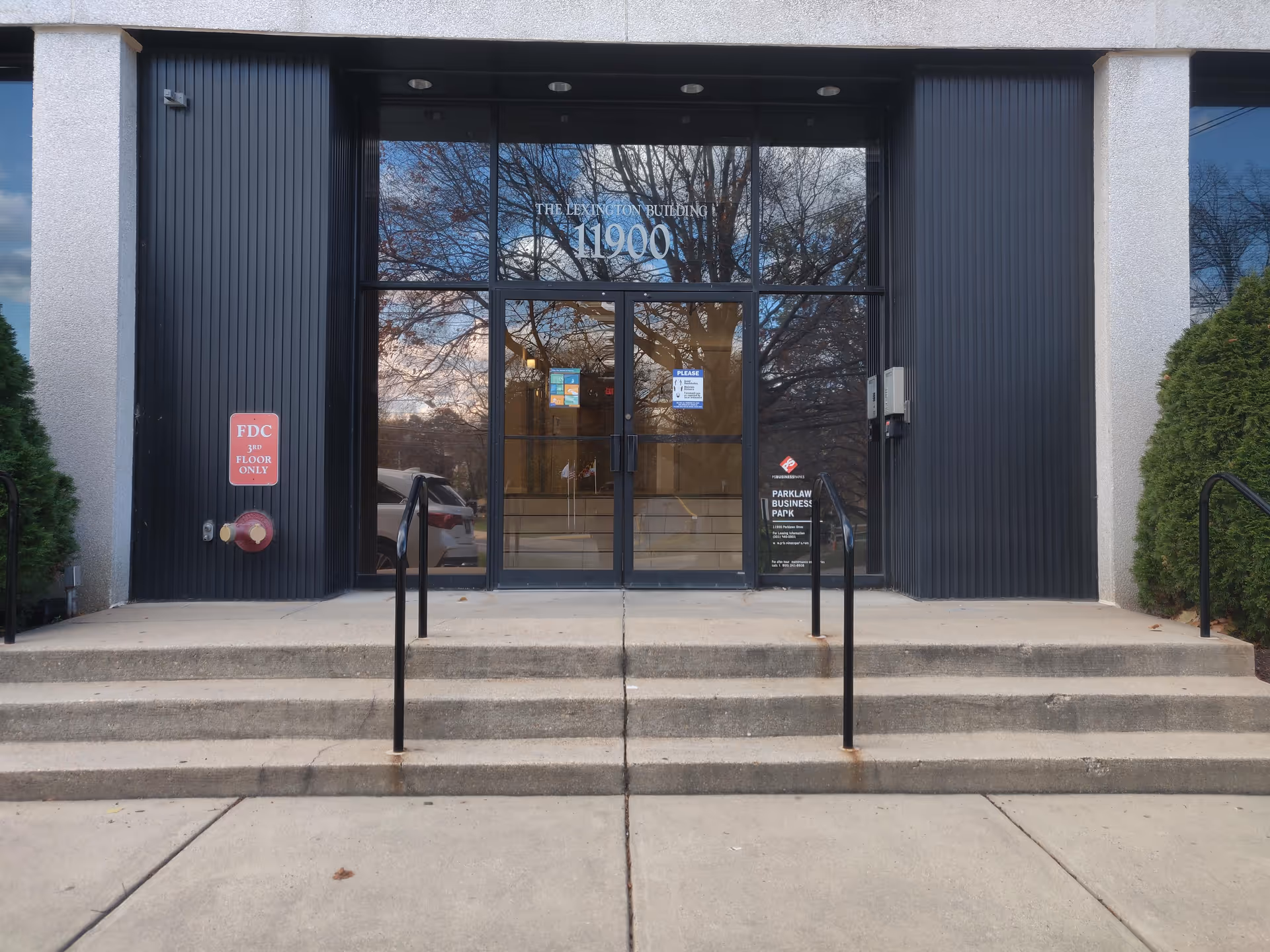 Exterior entrance to a building with glass doors, concrete steps, and surrounding landscaping.