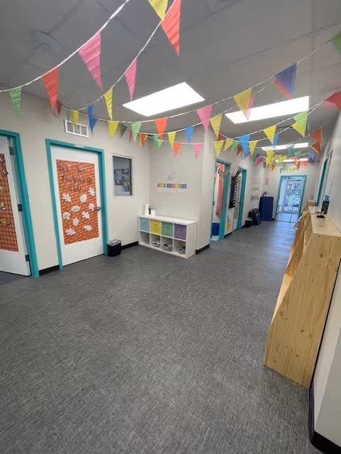 Bright interior hallway with colorful pennant banners, turquoise door frames, and cubby storage.