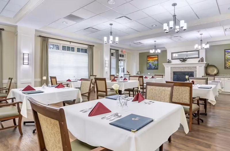 Bright dining room with tables dressed in white tablecloths and red napkins.