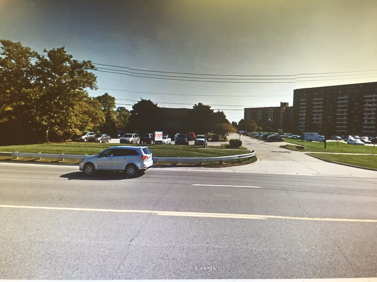 Wide road in foreground with a parking lot and a multi-story building to the right.