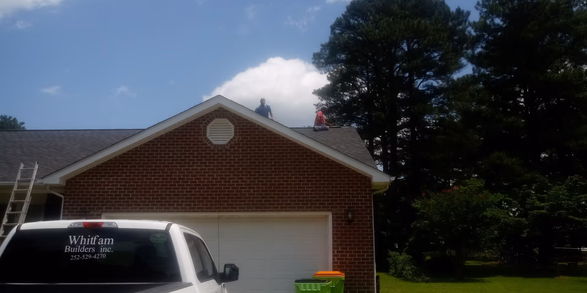Brick house exterior with two workers on the roof and a white pickup nearby.