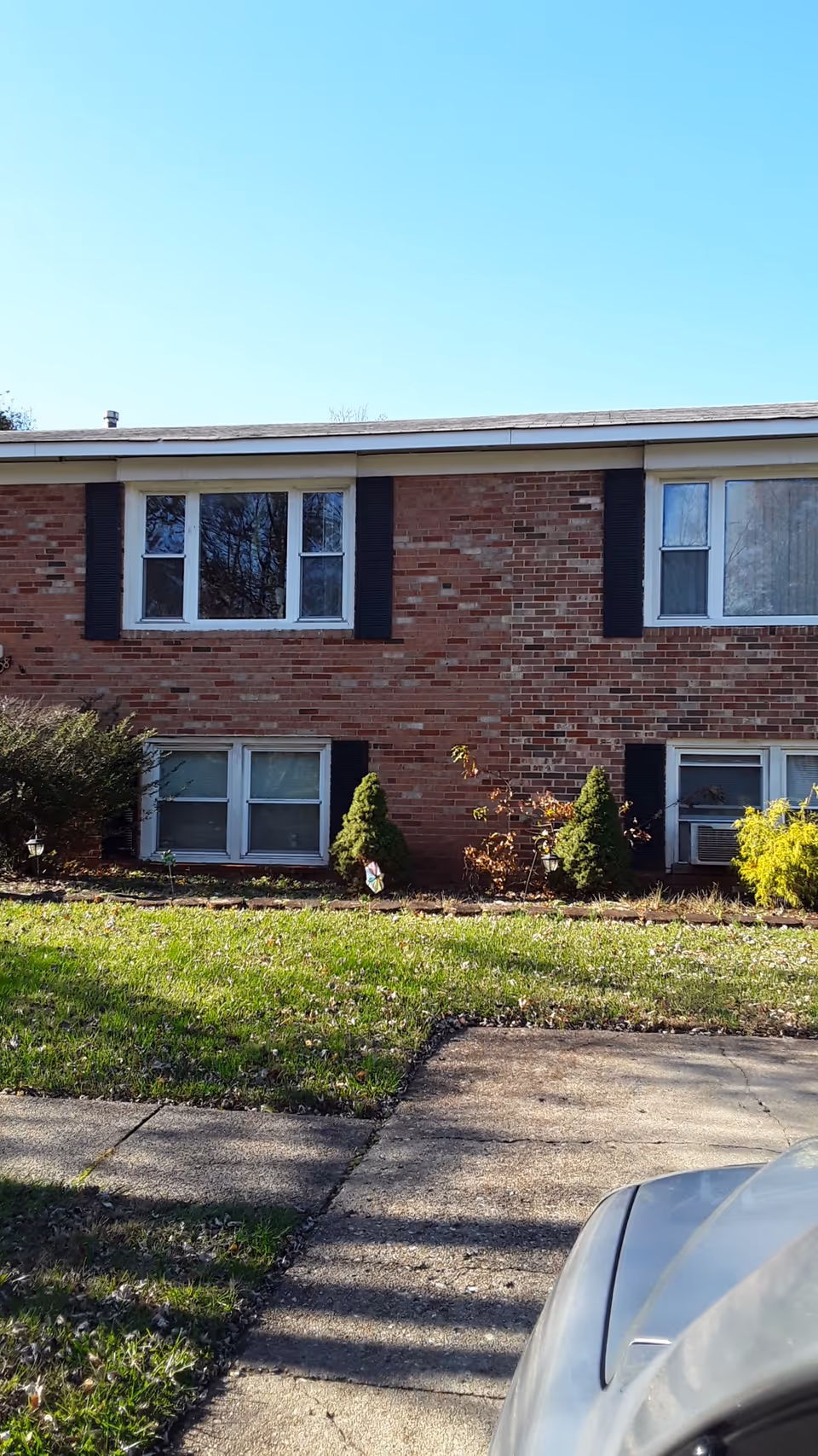 Exterior of a brick senior living building with windows, shrubs, and a parked car.