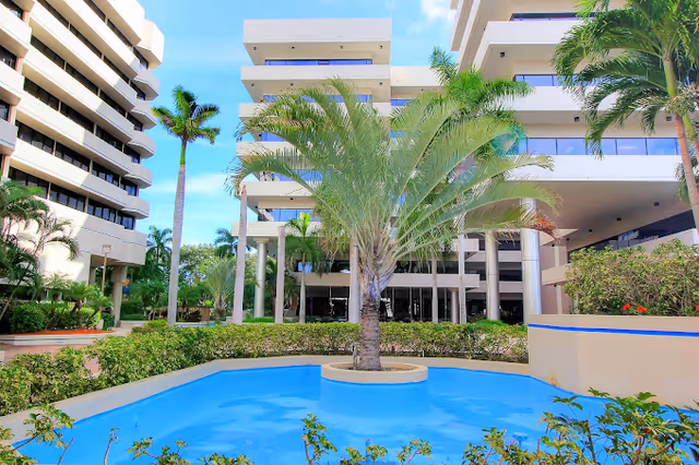 Exterior view of a modern multi-story senior living facility with a blue pool and palm trees.