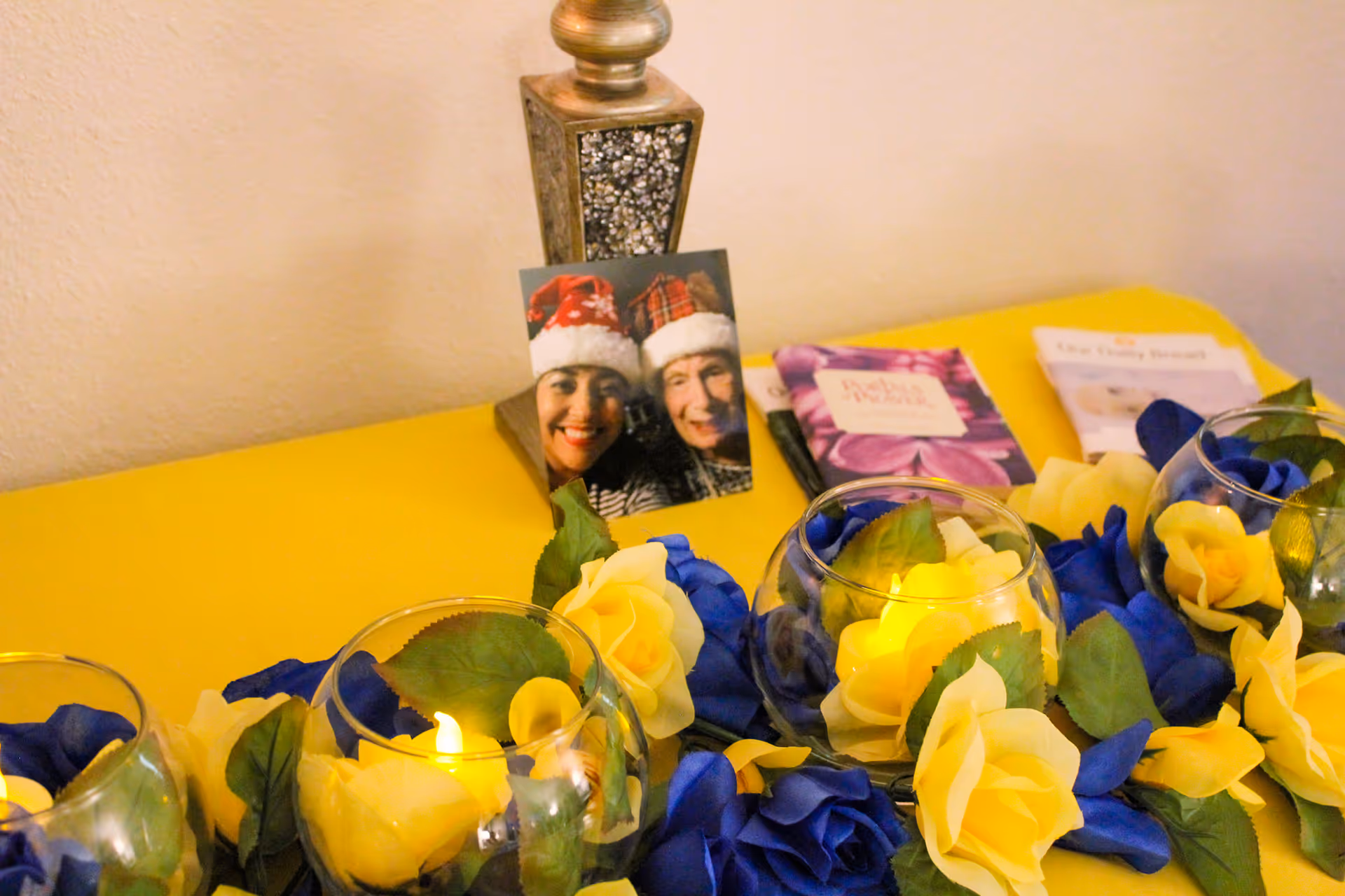 Decorative yellow table arrangement with blue-yellow flowers, candles, and a small photo display.
