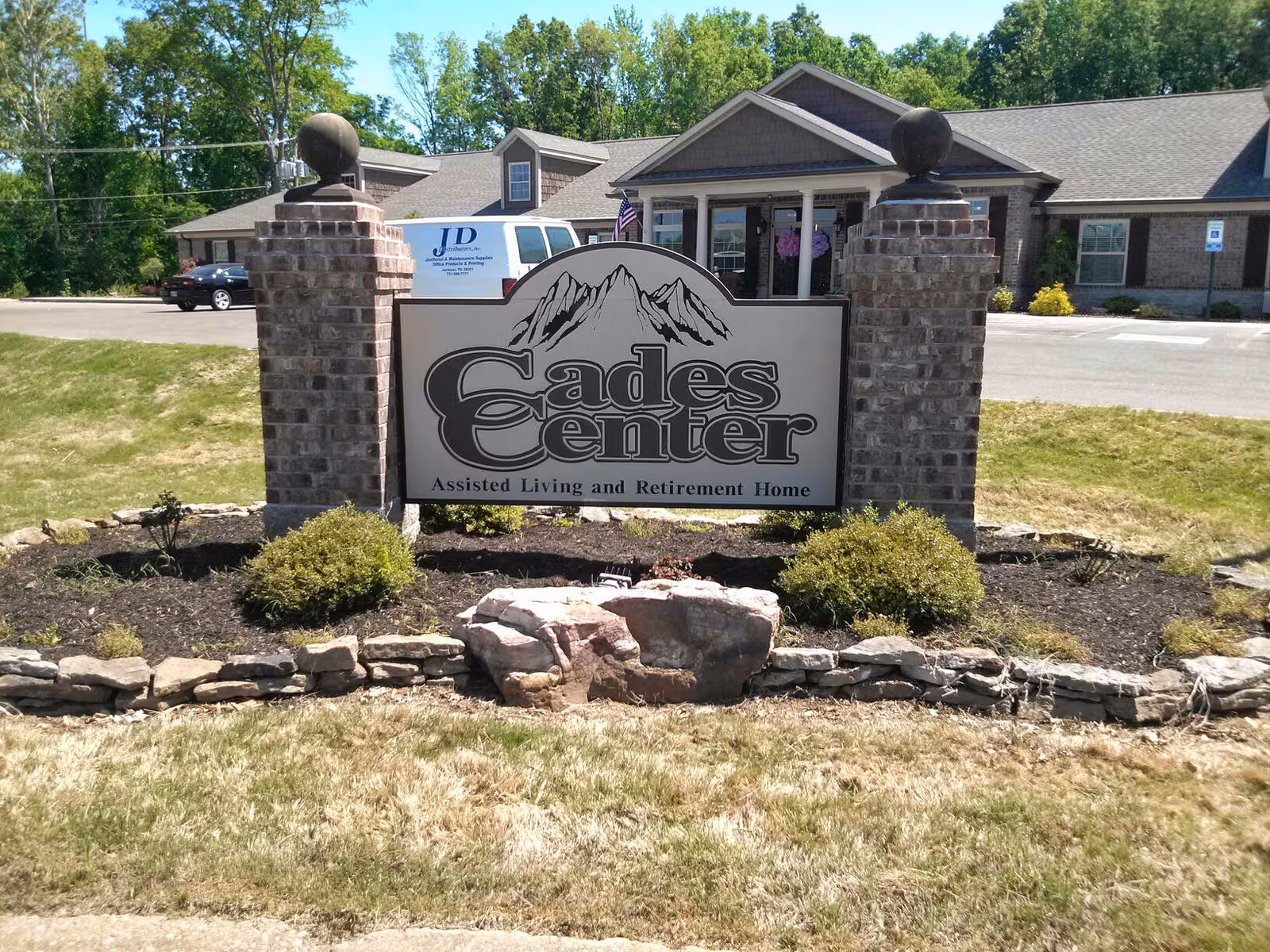 Entrance sign for Cades Center Assisted Living with brick pillars and a front building.