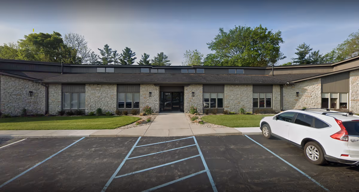 Single-story stone senior facility with a sidewalk, landscaping, and a white car in the parking lot.