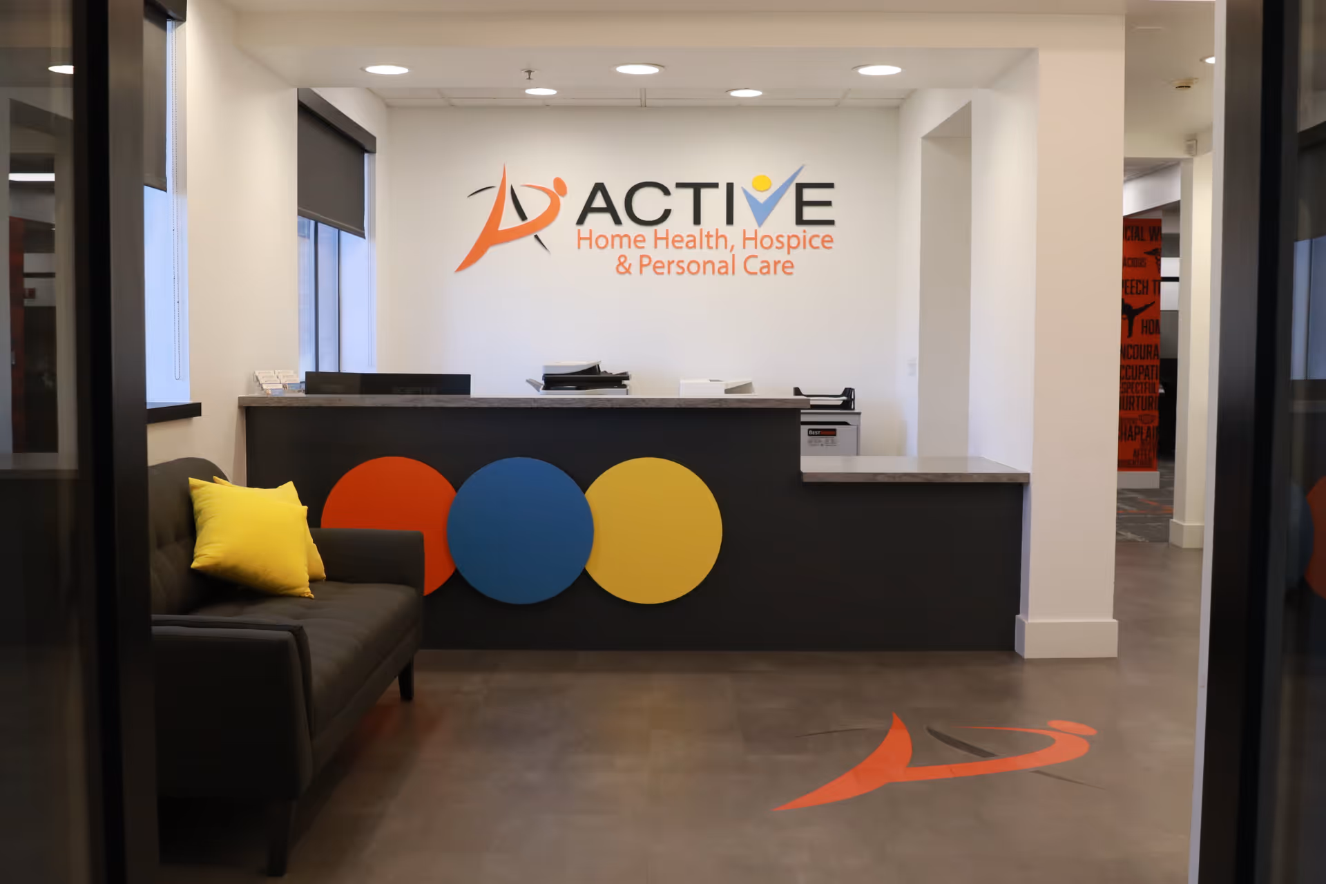 Reception lobby with a dark front desk, couch, and colorful circular decor around the Active logo.