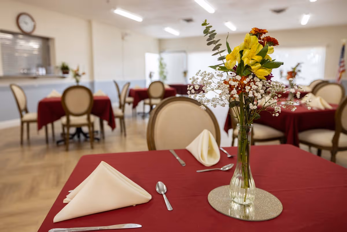 A dining room in a senior facility with red tablecloths and floral centerpieces.